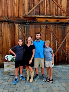 A man and woman standing in front of a wood door with two younger boys.