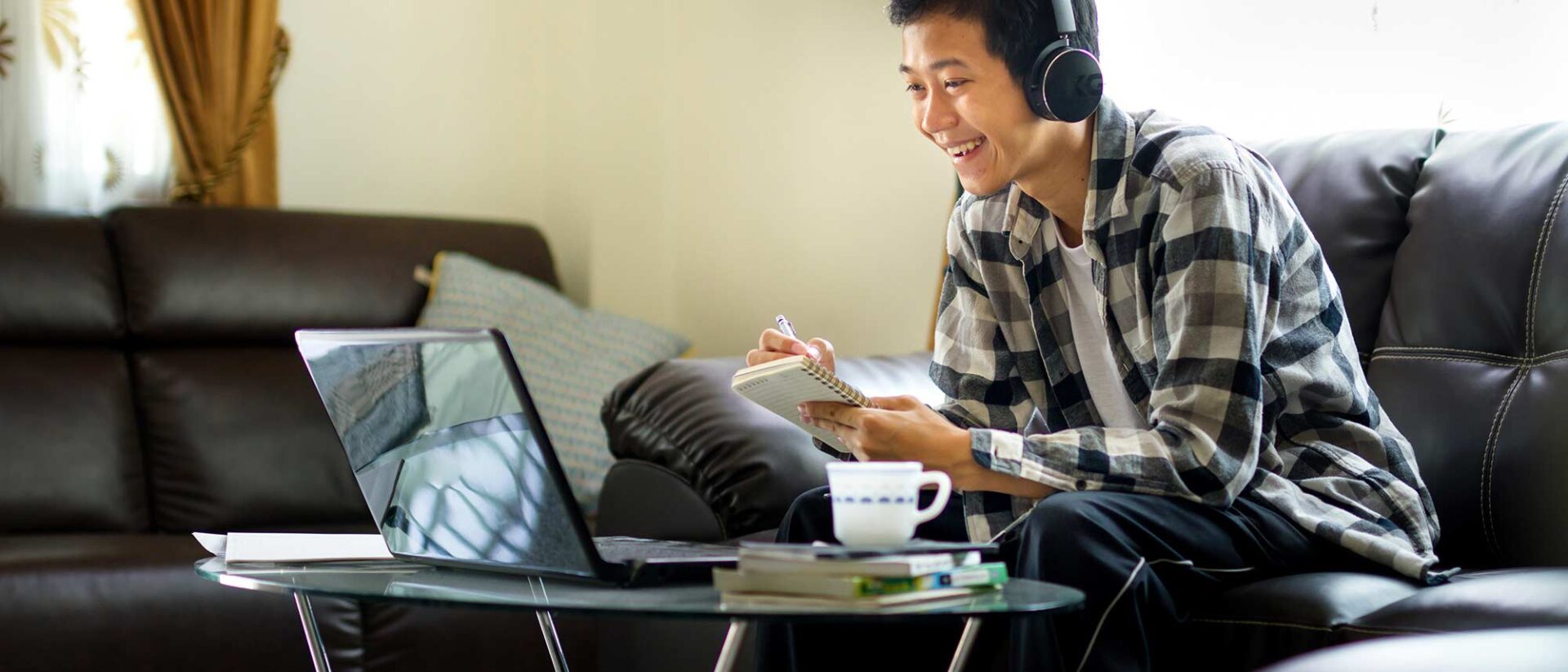 Student with his headset on and taking notes during an online class